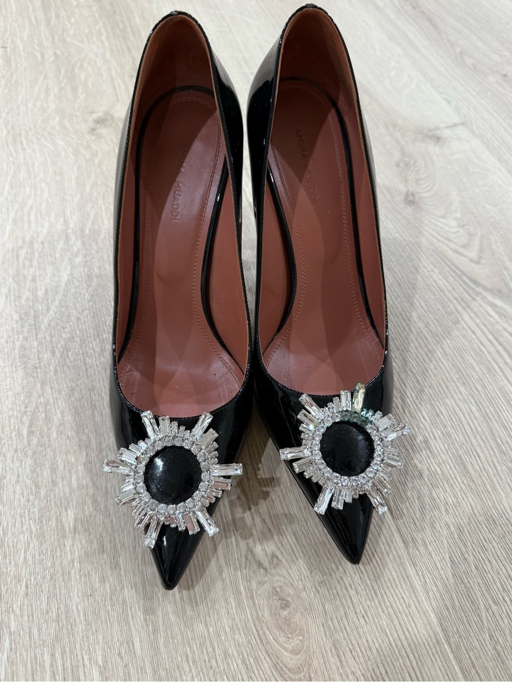 Amina Muaddi Black Patent Pointed Toe Pumps with Crystal Sunburst Brooch